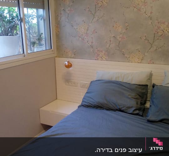מיטה עם כריות כחולות וטפט פרחוני על הקיר